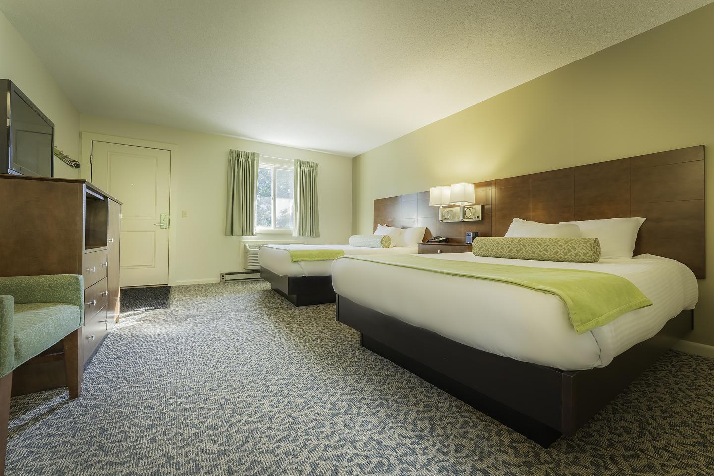 Hotel room with two beds, green accents, and a window.