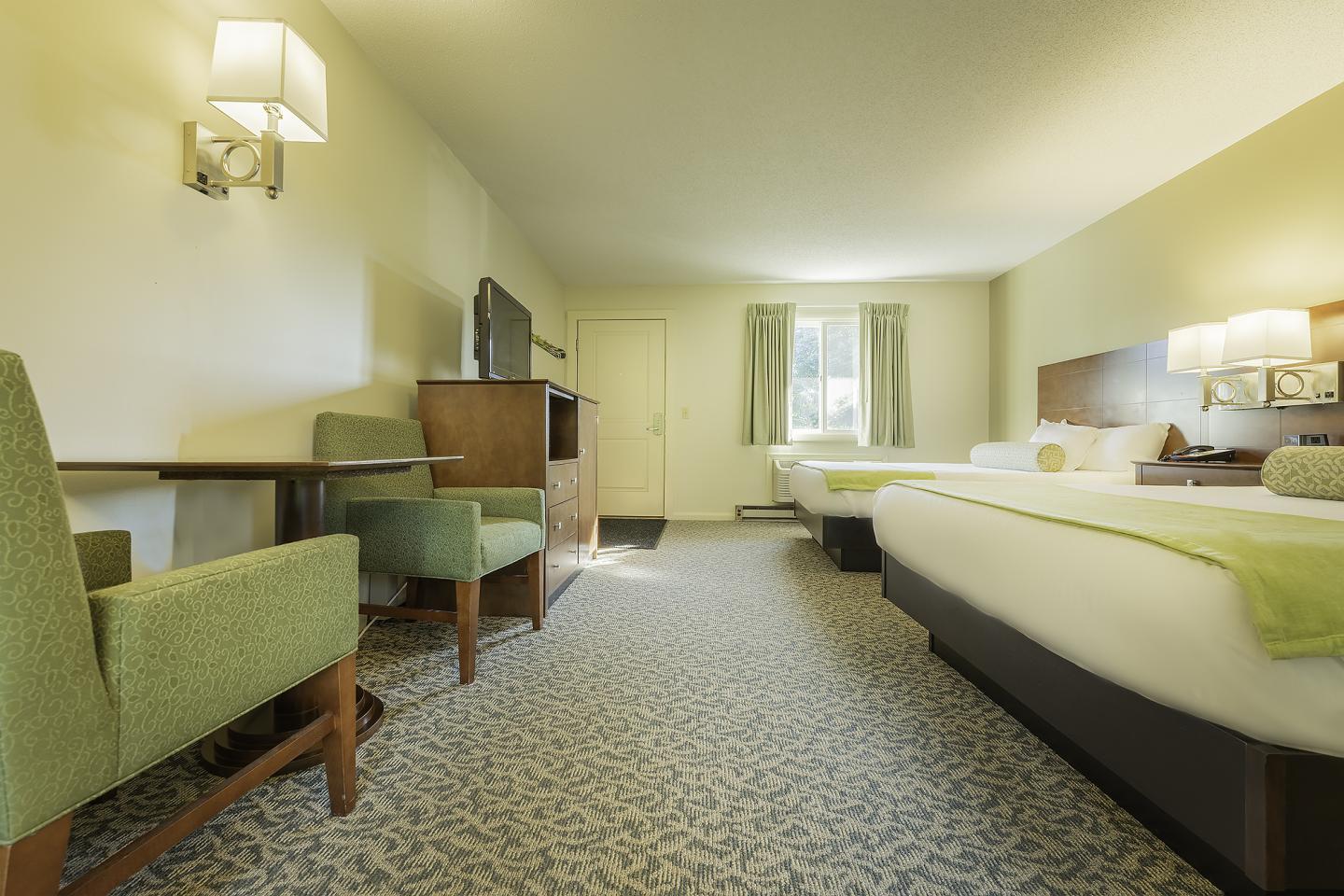 Spacious hotel room with two beds and green accents, soft lighting.