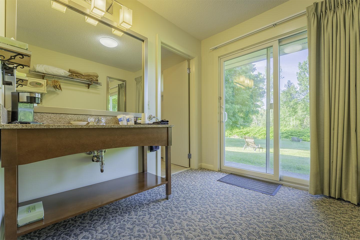 Hotel room with open sliding door, leading to a lush garden view.