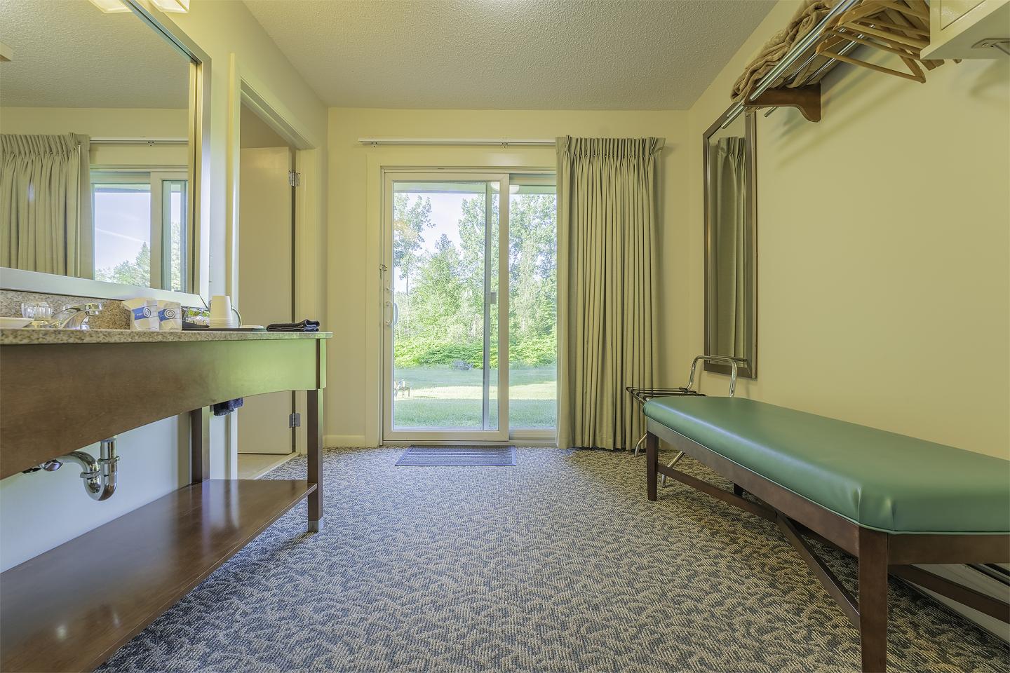 Changing room with a bench, mirror, and view of grassy area through glass door.