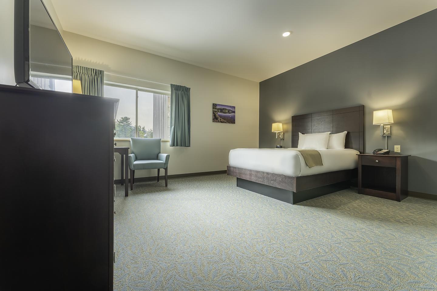 Spacious hotel room with a large bed, two lamps, and a window with curtains.