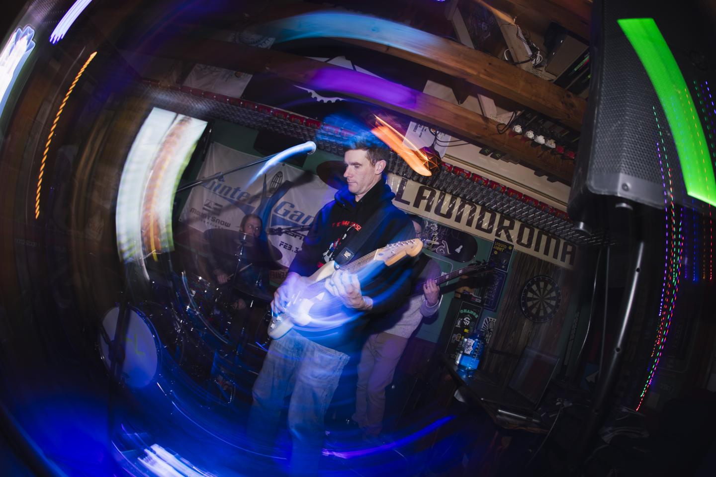 Musician plays electric guitar on stage with colorful lighting effects.