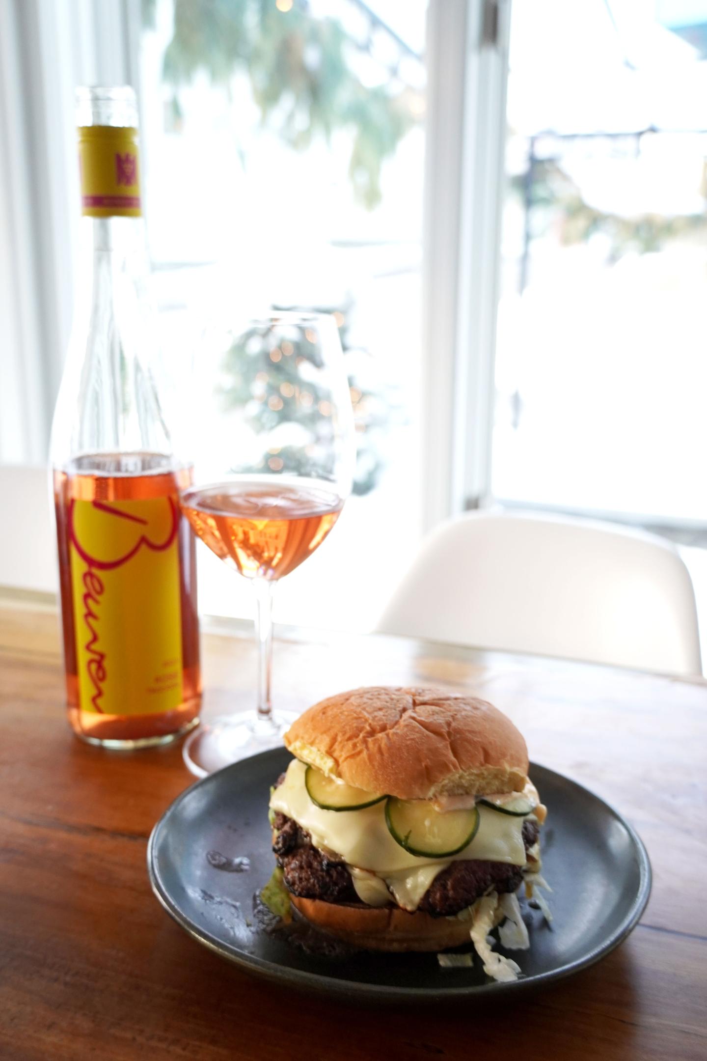 Burger and glass of rosé wine on a table with a wine bottle.