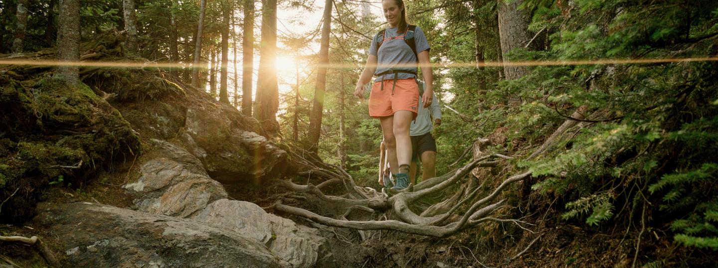 Hiker on a forest trail at sunset, wearing orange shorts and a backpack.