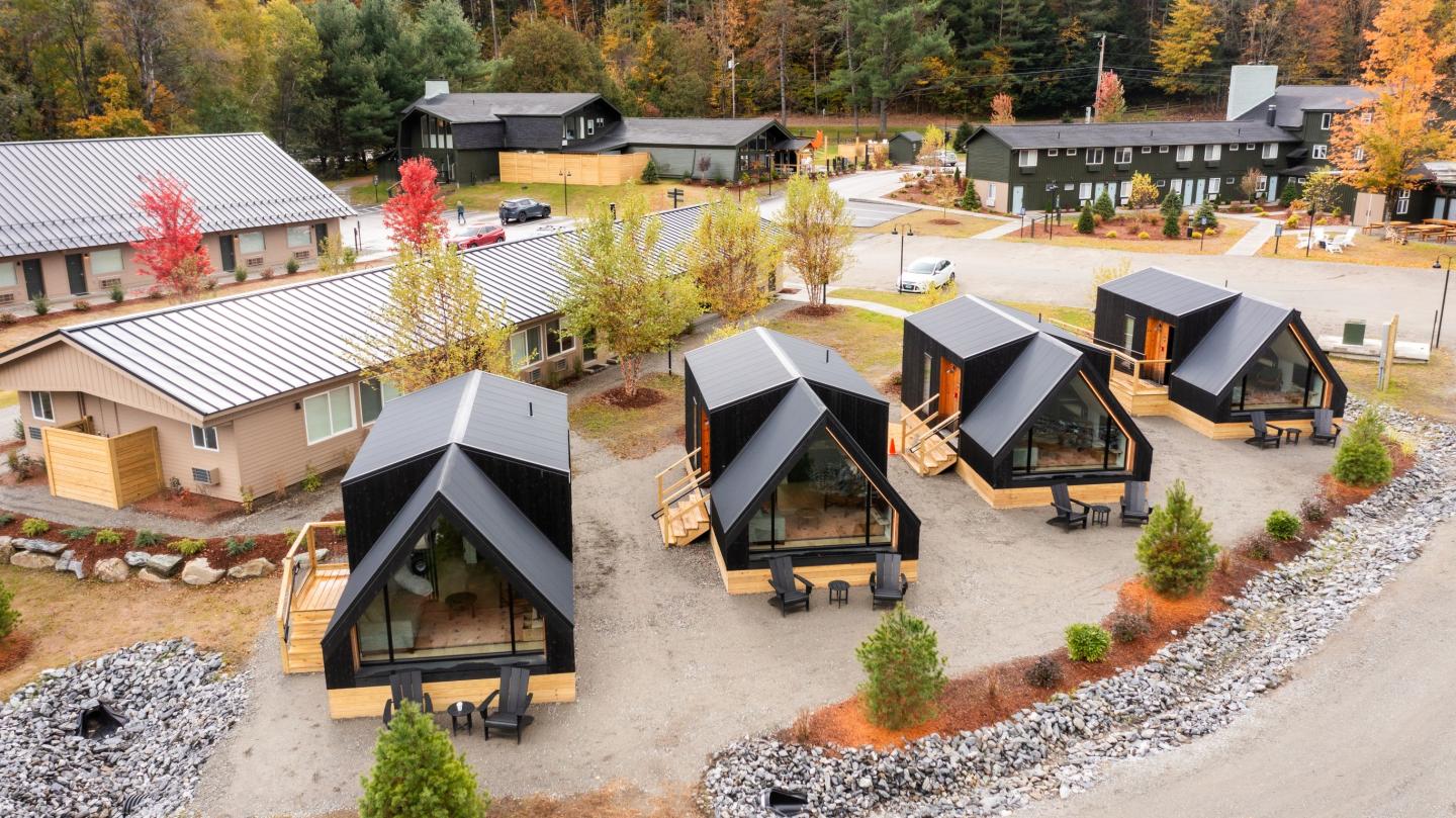 Modern cabins with black roofs in a wooded setting, surrounded by autumn trees.
