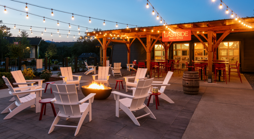 Outdoor patio with string lights, fire pit, and white chairs in evening light.
