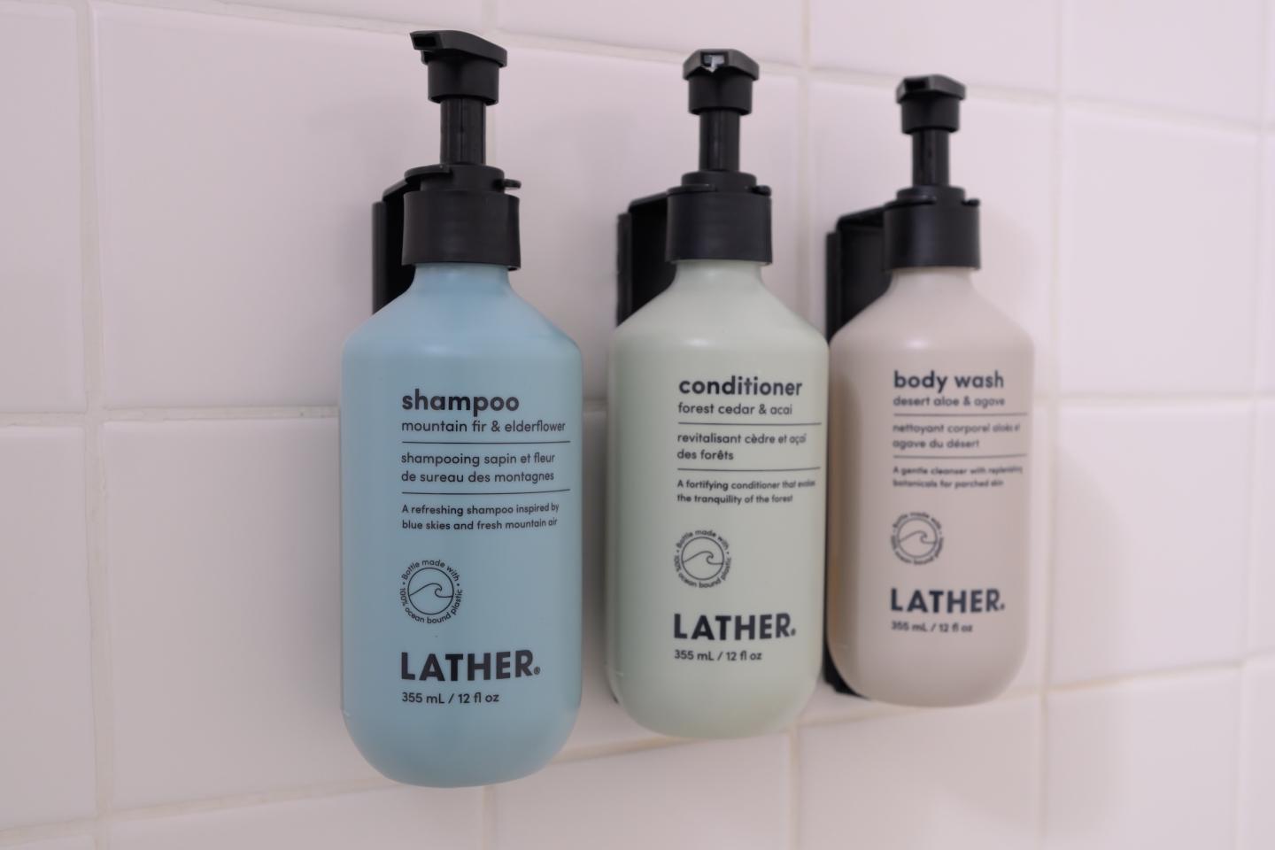 Three Lather bottles: shampoo, conditioner, body wash, mounted on a tiled wall.