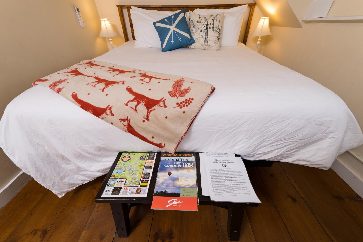 Cozy bed with white linens, red patterned blanket, and decorative pillows.