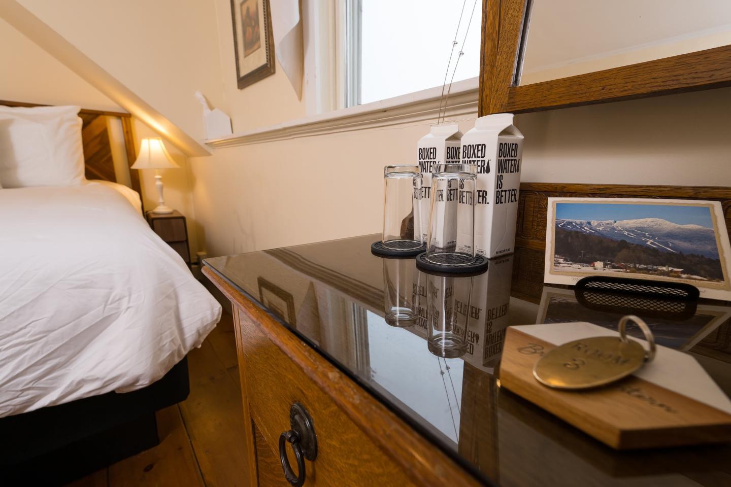 Cozy hotel room with tidy bed, wooden dresser, and scenic mountain photo.
