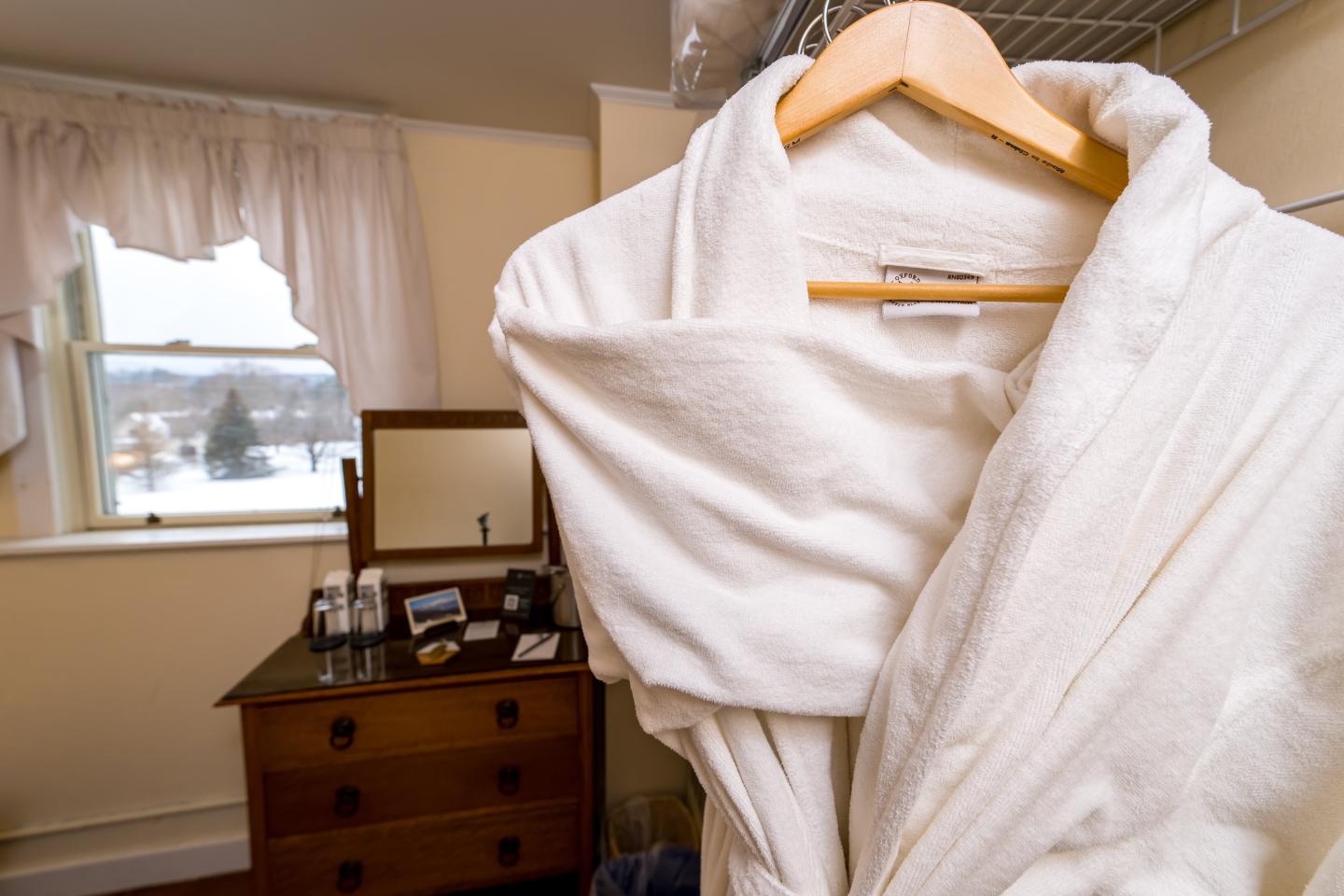 White bathrobe on a hanger, dresser and snowy window in the background.