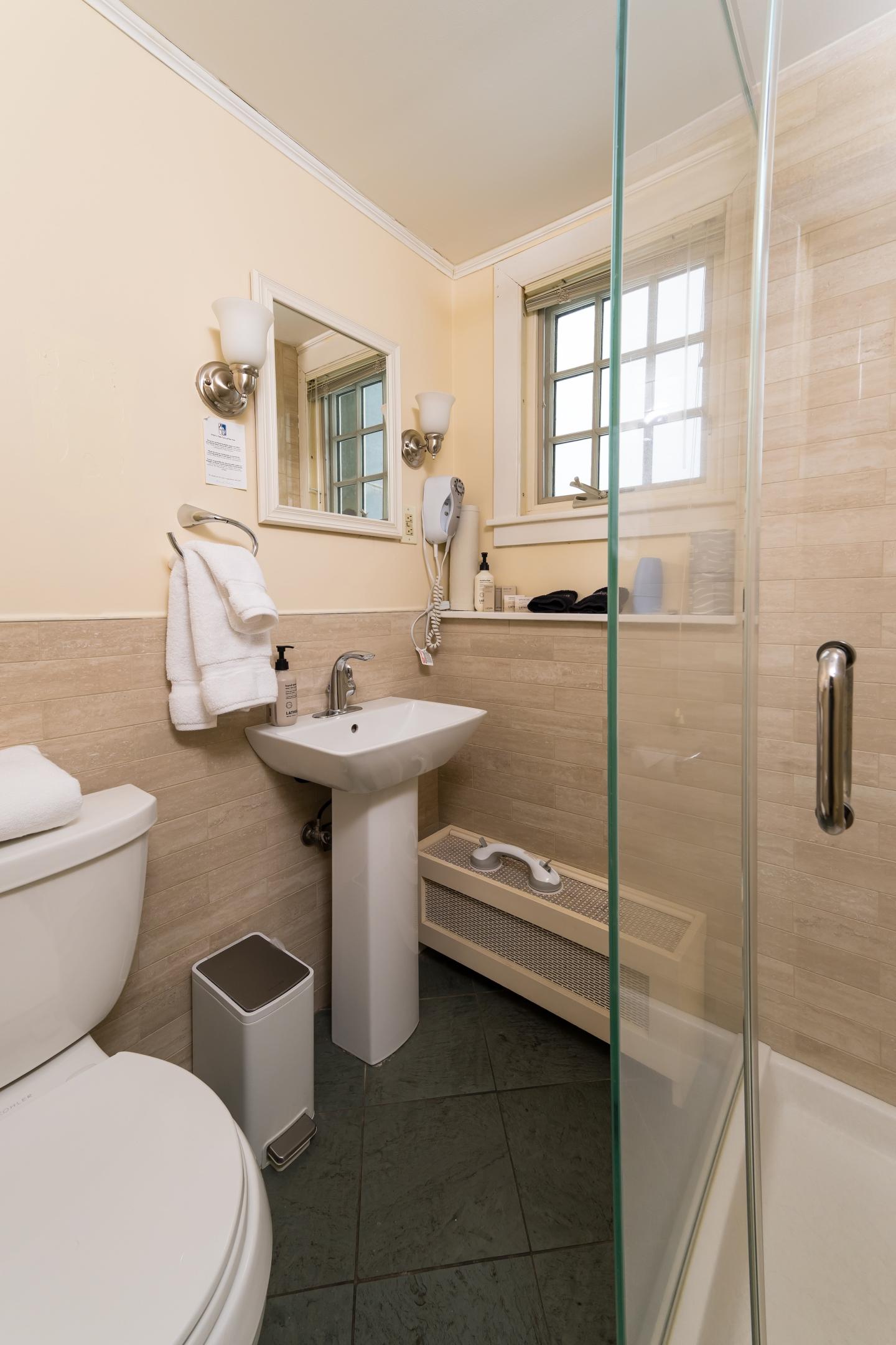 Compact bathroom with a shower, toilet, and sink; neutral tones and a window.