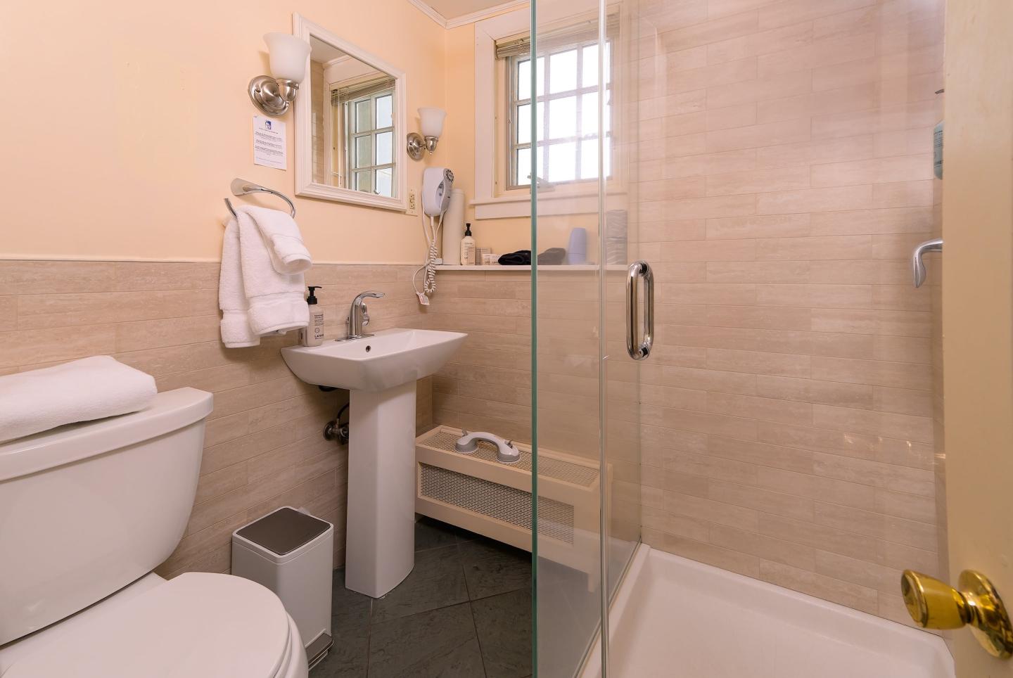 Small bathroom with a glass shower, sink, and toilet, beige tiles.