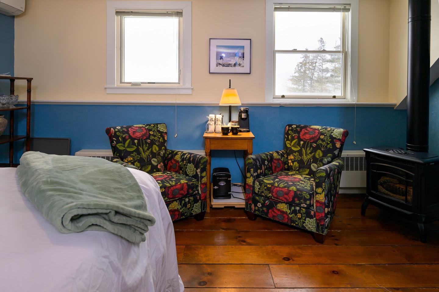 Cozy room with floral chairs, lamp, bed, and folded towels.