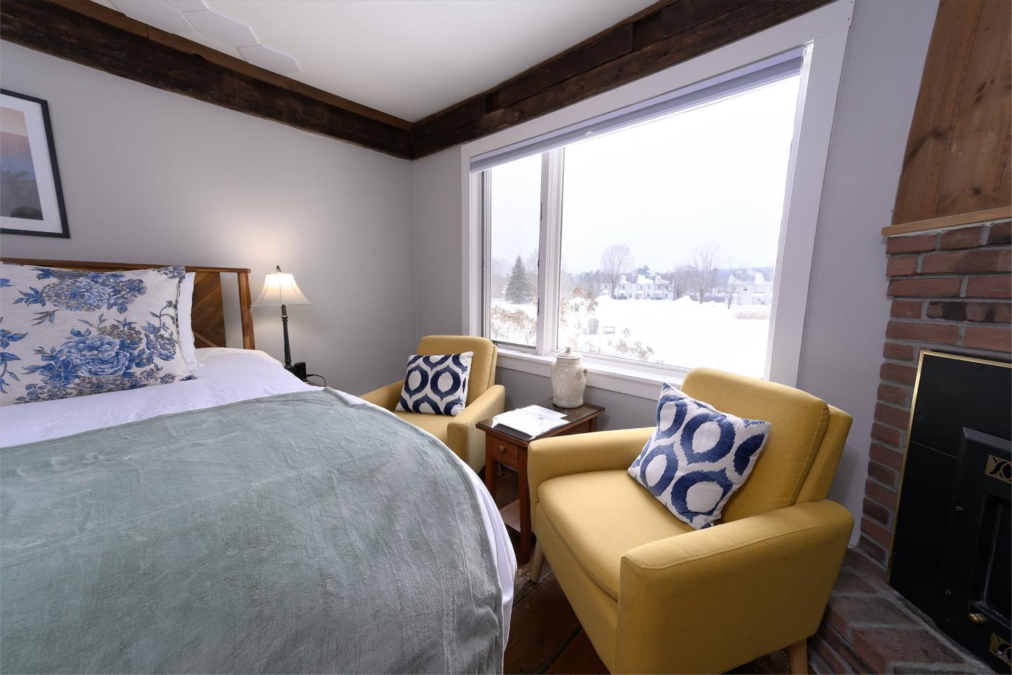 Cozy bedroom with yellow chairs, a bed, and a window view of snow.