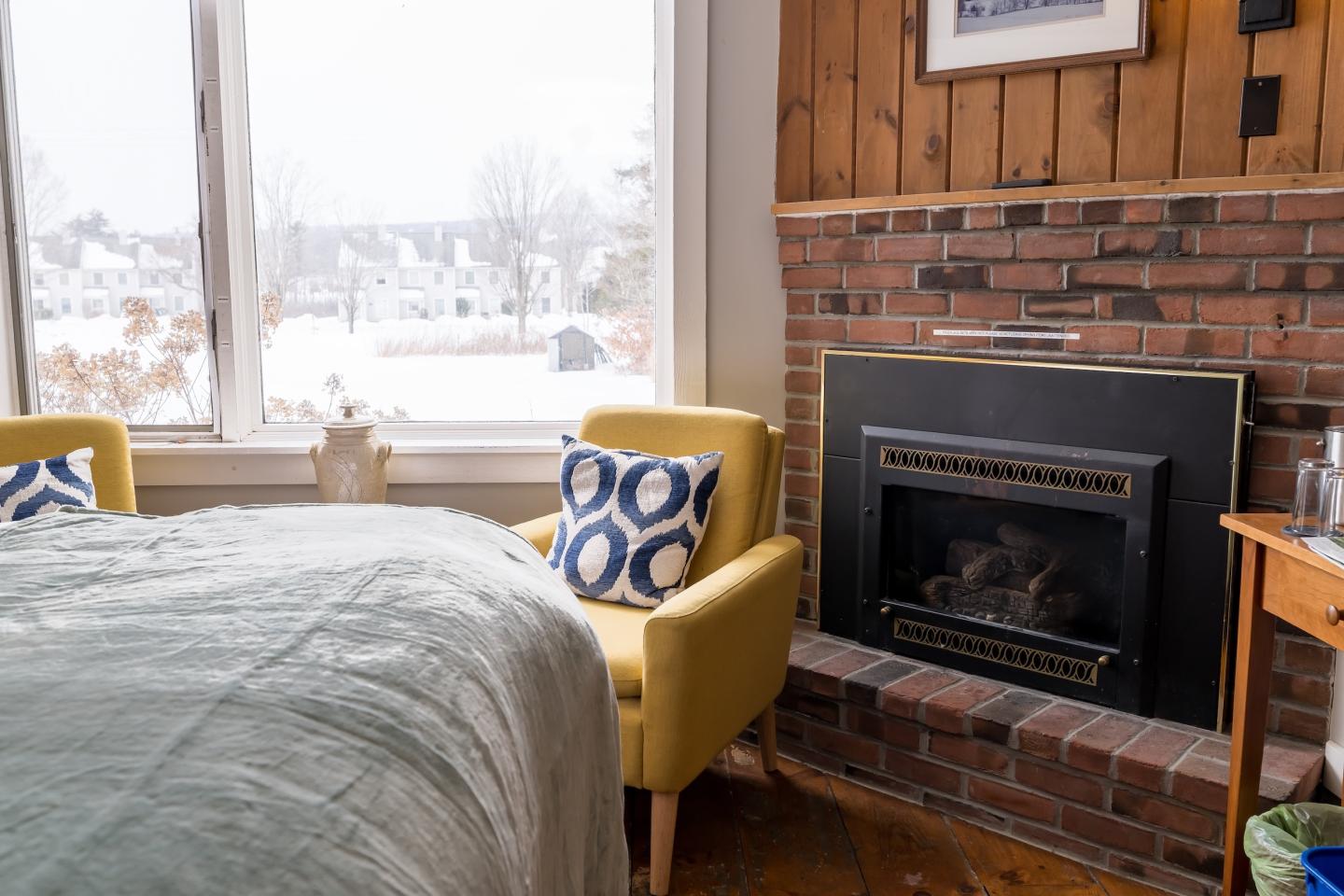 Cozy room with yellow armchairs, a fireplace, and snowy view outside.