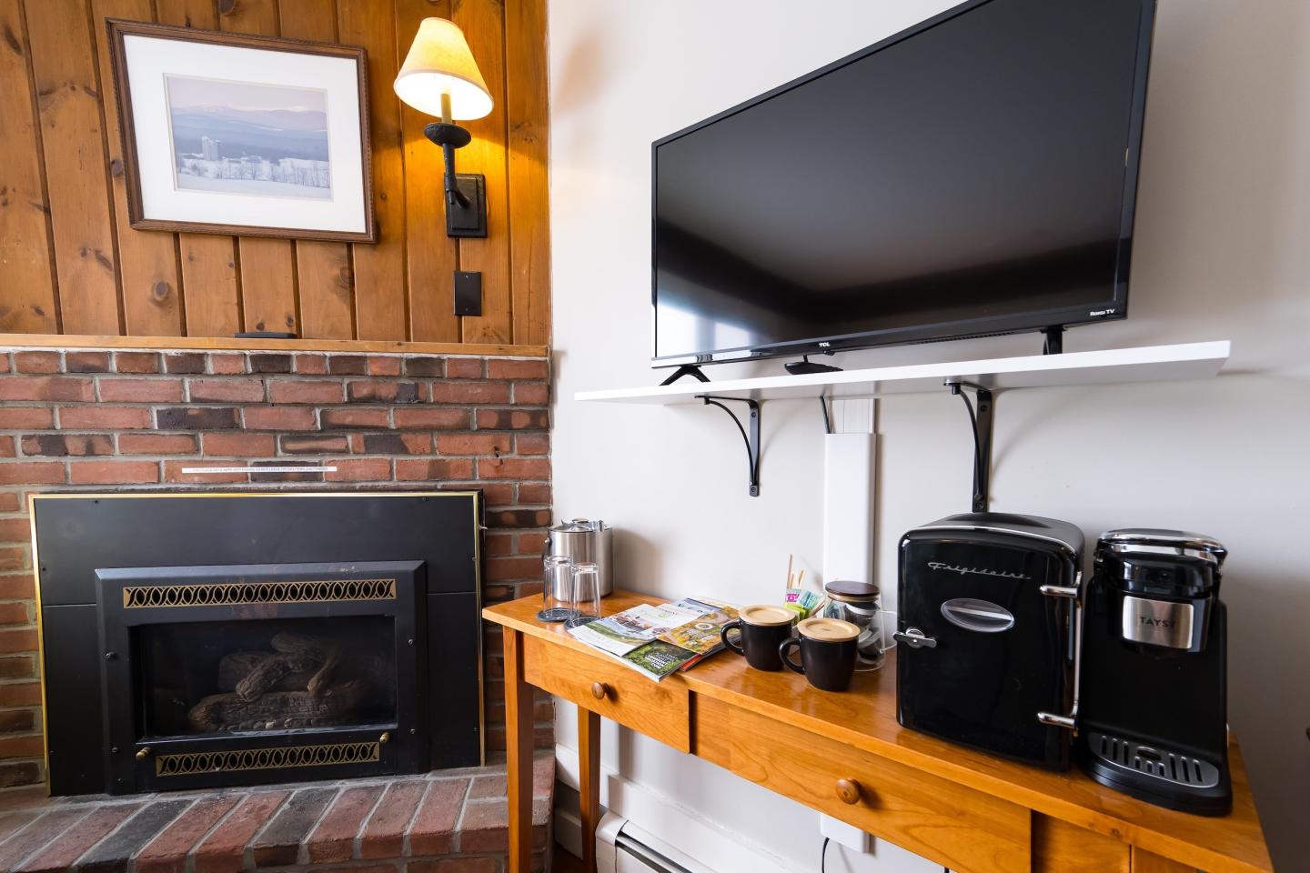Cozy room with a fireplace, wall-mounted TV, and coffee maker on a wooden table.