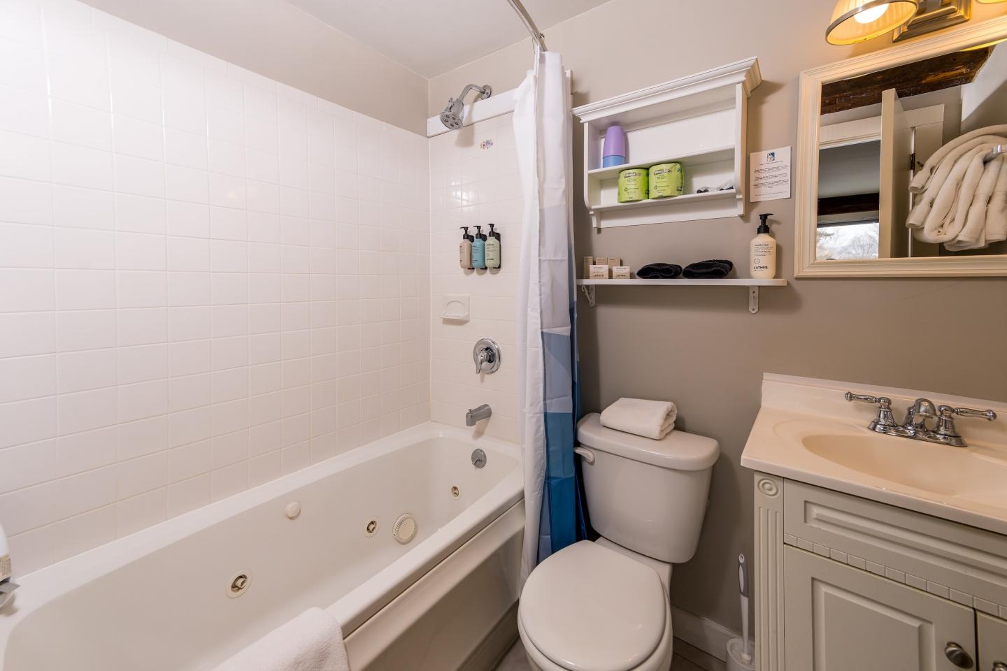 Bathroom with tub, shower curtain, toilet, sink, and shelves.