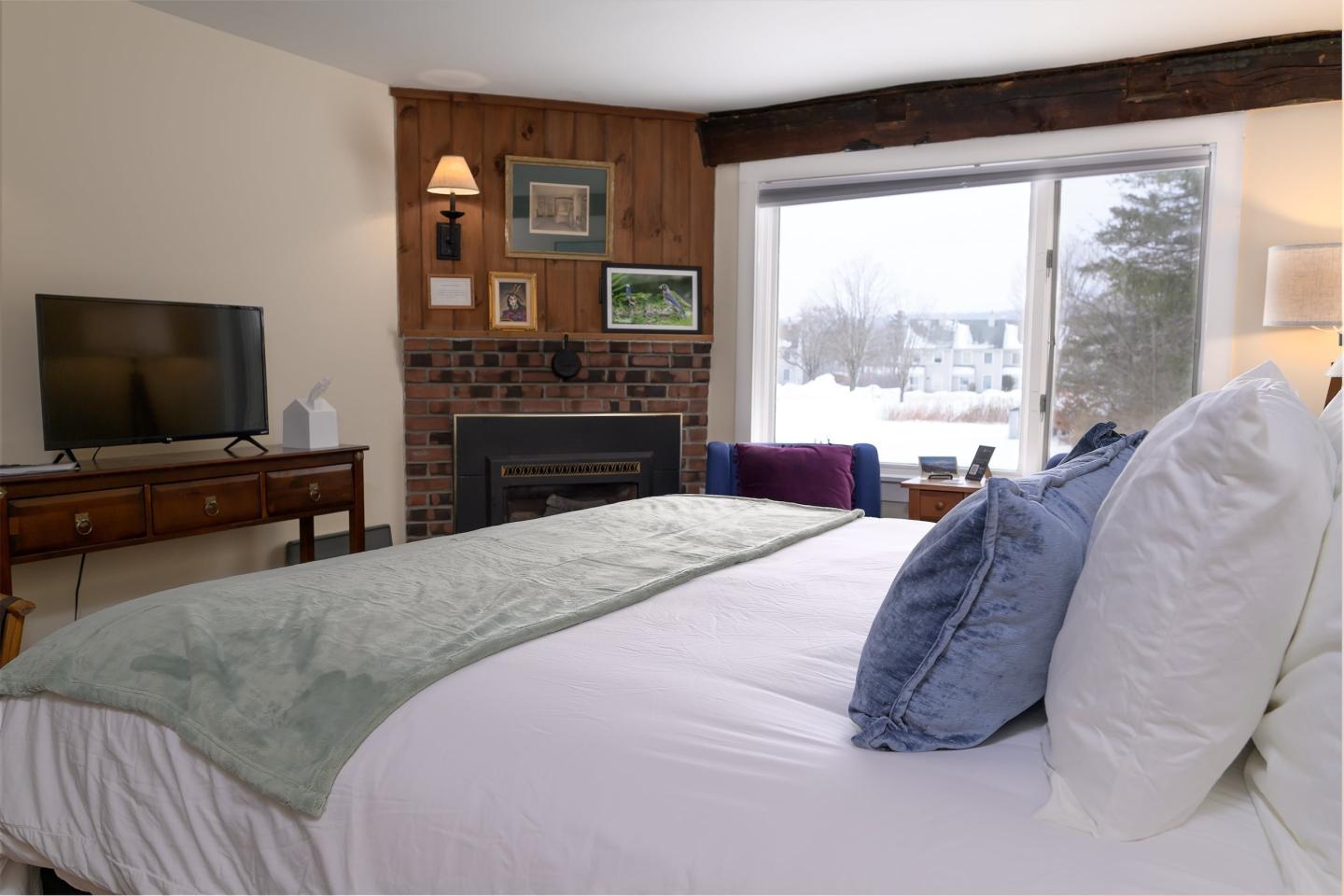 Cozy bedroom with a large bed, TV, fireplace, and window overlooking snowy scenery.