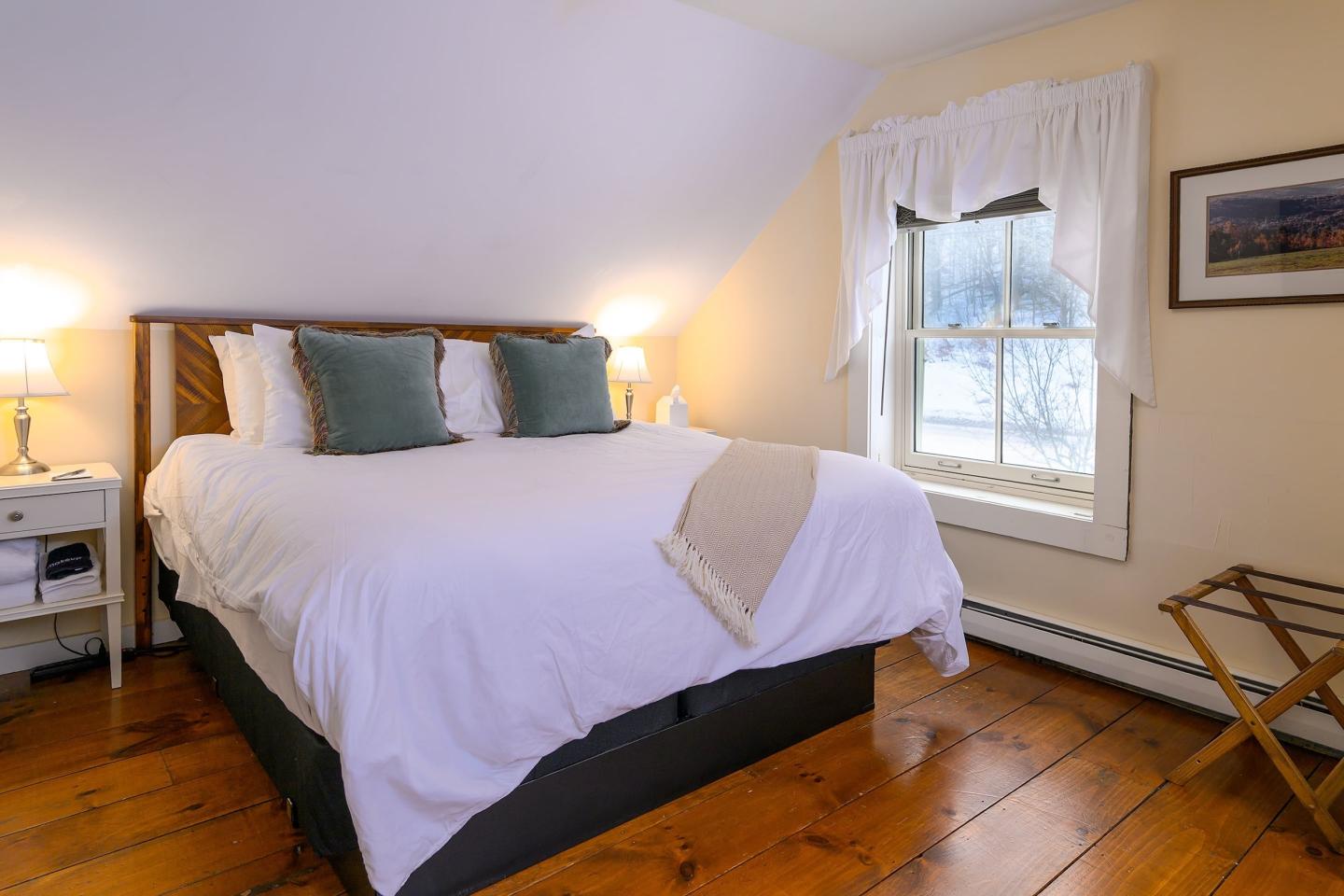 Cozy bedroom with a large bed, wooden floor, and a window with curtains.