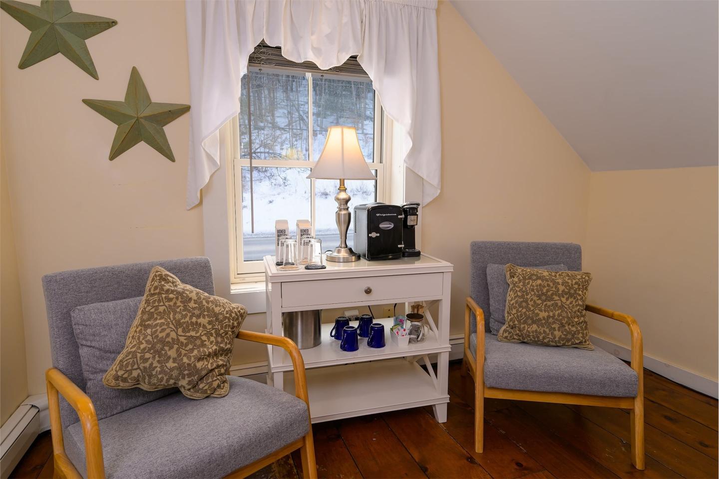 Cozy room with two chairs and a window. Table has coffee maker and mugs.