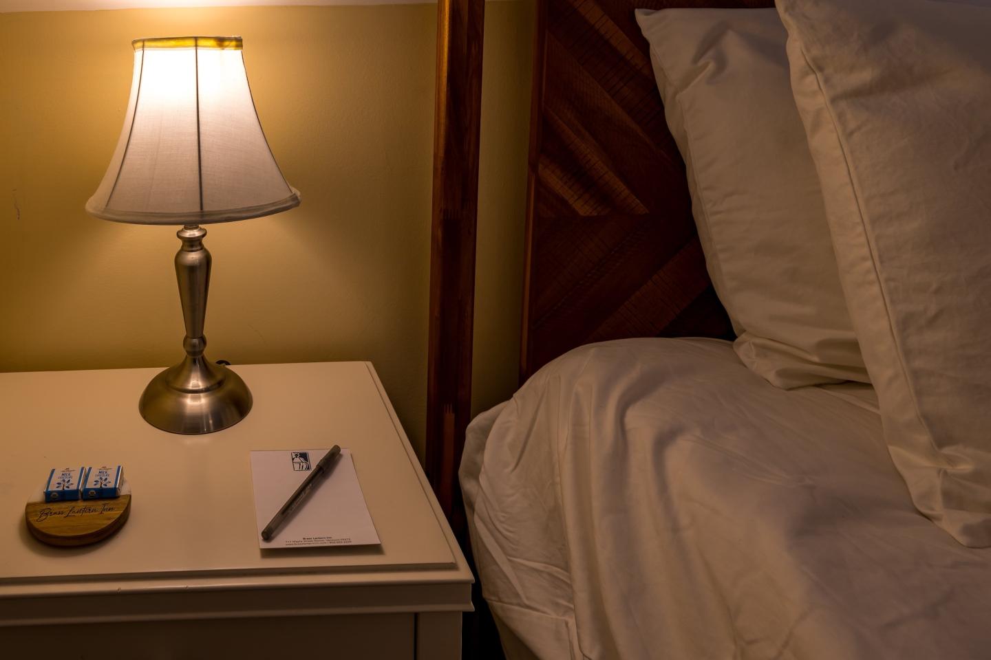 Bedside table with lamp, notepad, and snacks beside a bed.