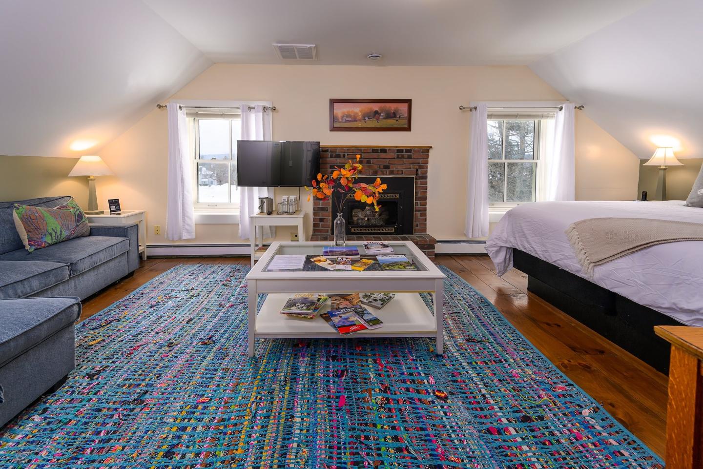 Cozy attic room with colorful rug, sofa, fireplace, and bed.