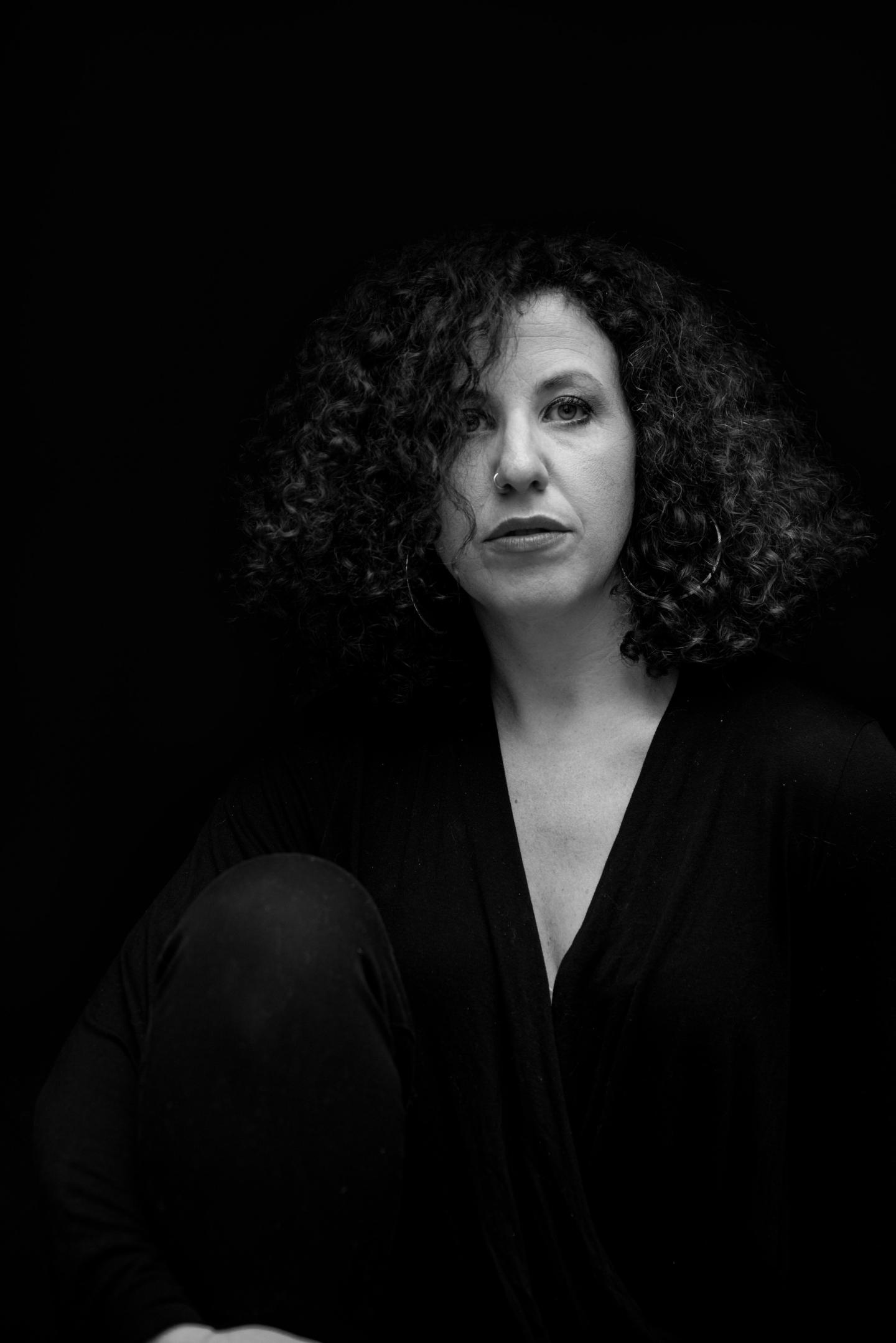 Black and white portrait of a woman with curly hair, wearing dark clothing.
