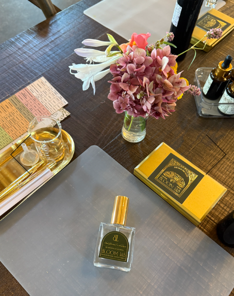 Perfume bottle, pink flowers, and gold box on wooden table.