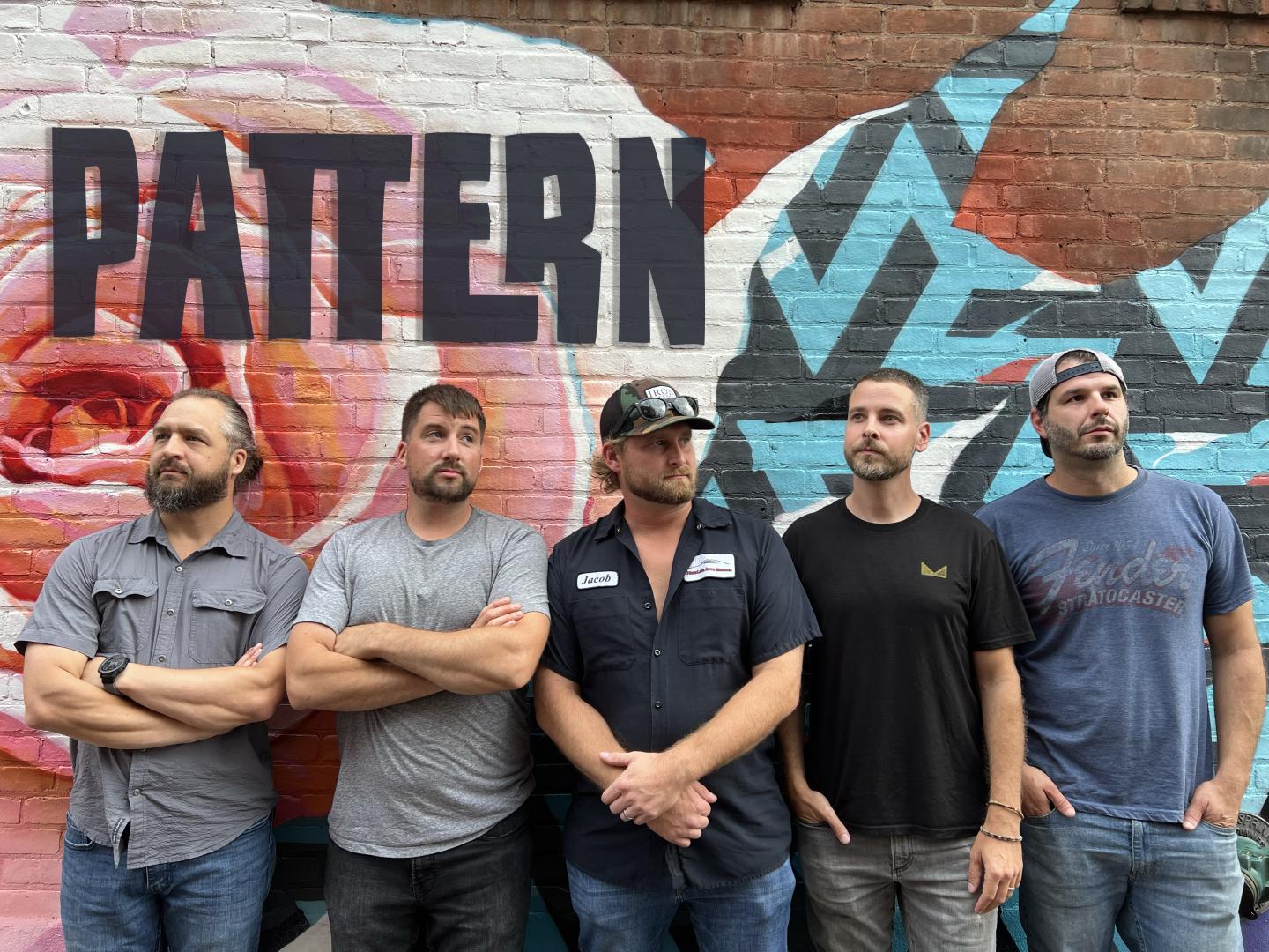 Five men stand in front of a colorful mural wall.