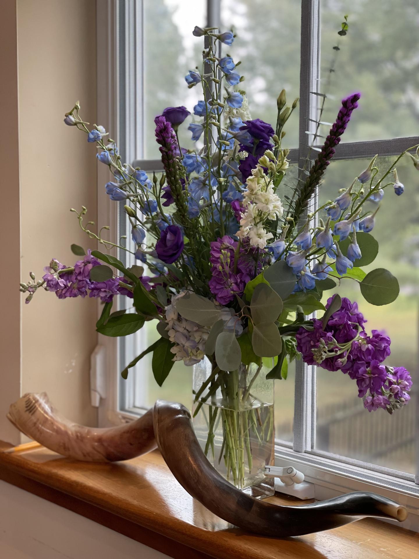 Vase of purple and blue flowers on a windowsill with two curved horns.