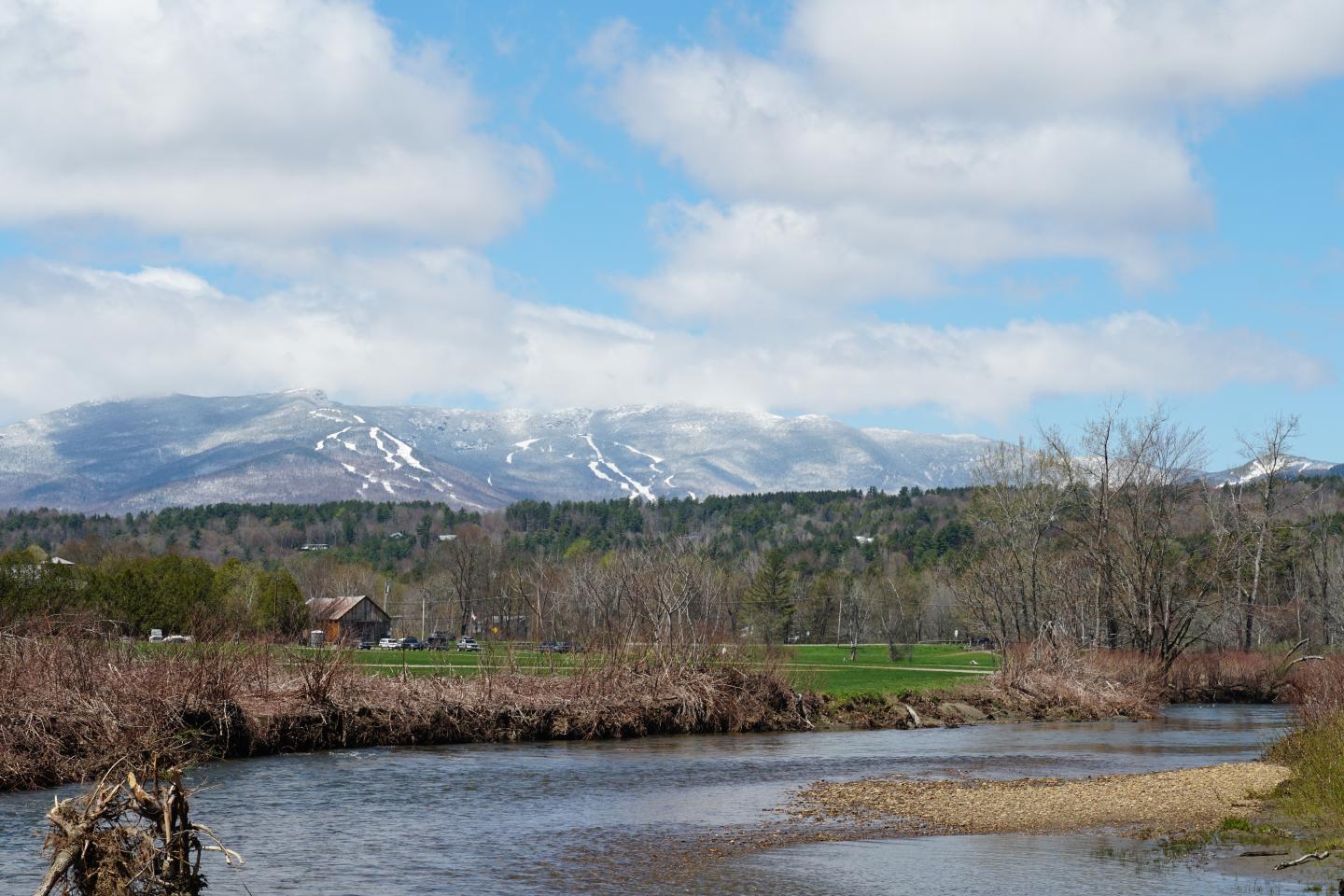 River winding through a green valley with snow-capped mountains and clouds.