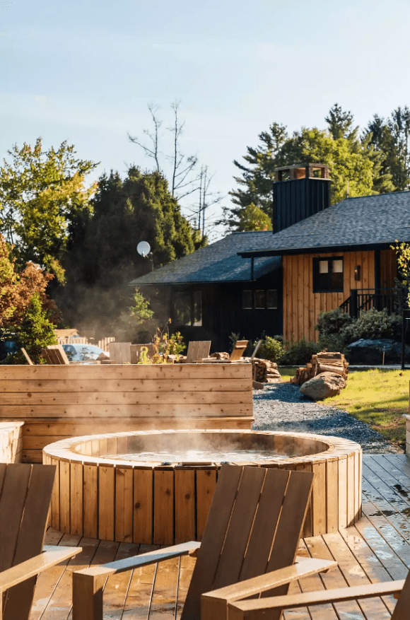 Steaming outdoor hot tub with wooden chairs on a sunny day.