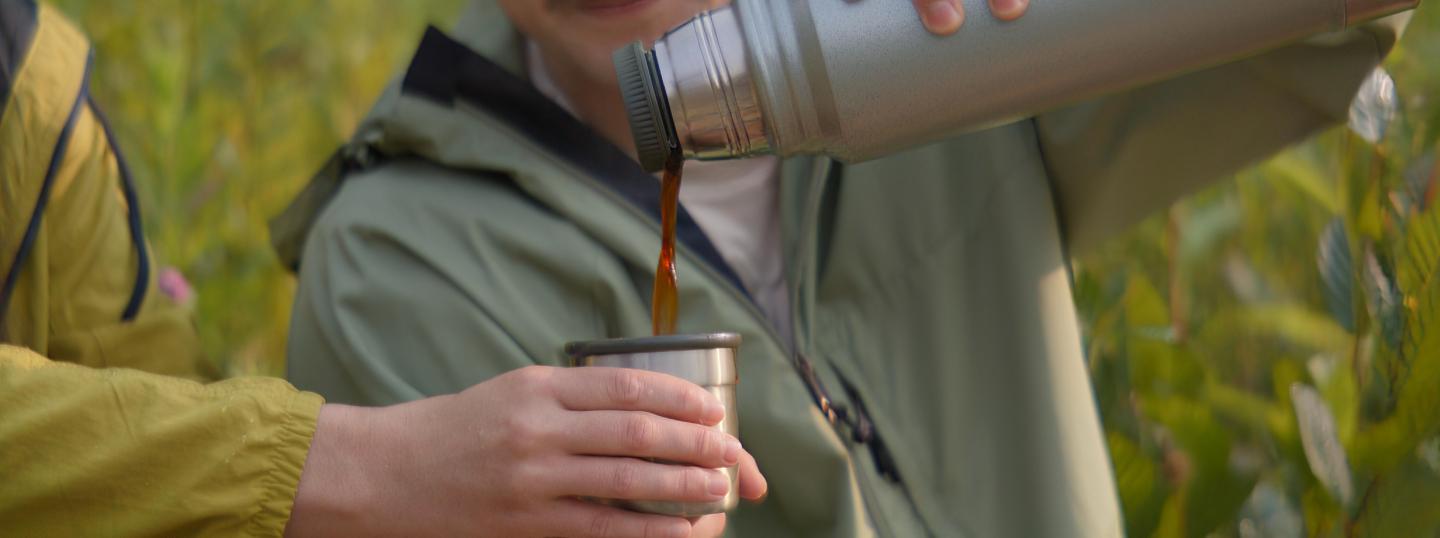 Pouring coffee from a thermos into a cup outdoors.