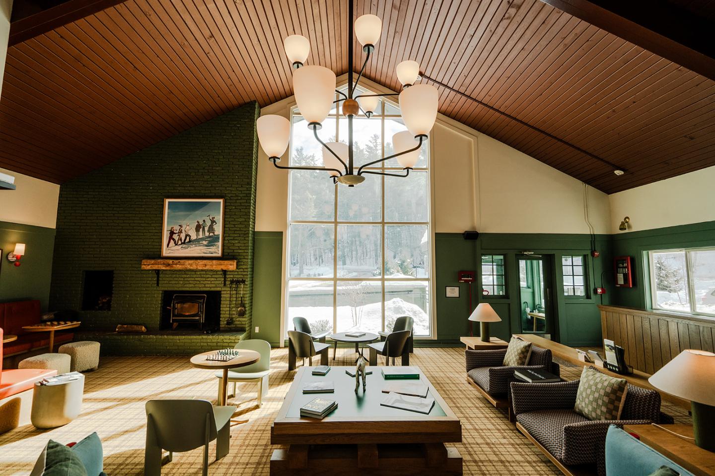 Cozy lounge with large windows, green walls, armchairs, and a chandelier.