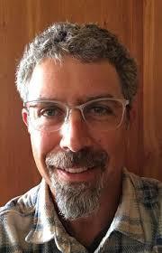 Man with glasses and gray hair smiling warmly in a plaid shirt.