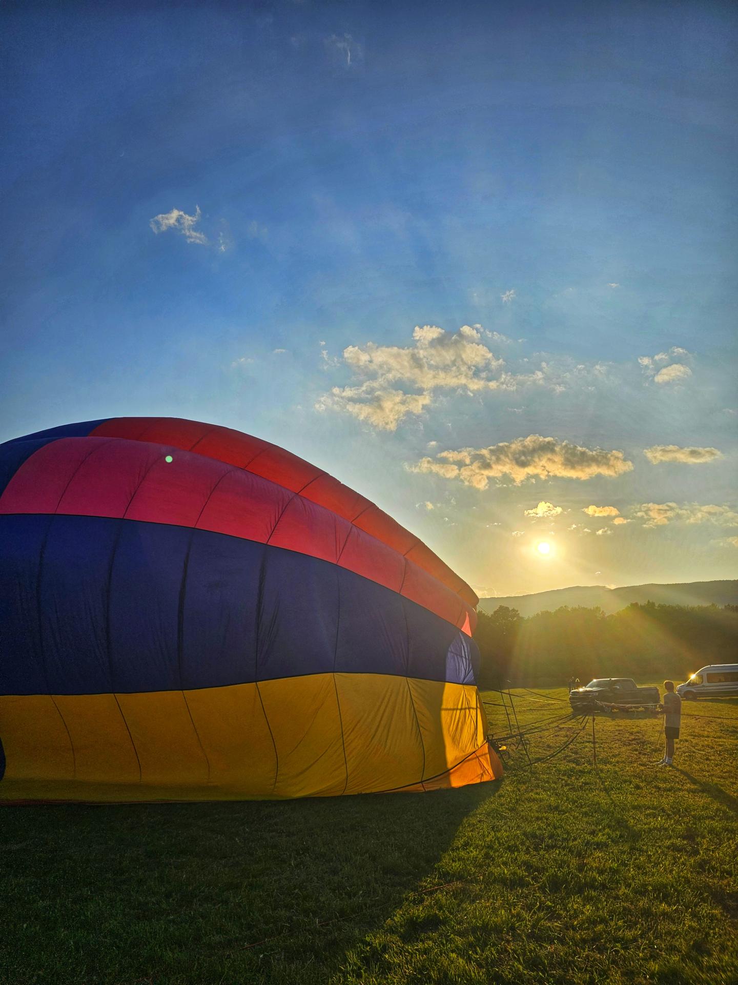 Deflated hot air balloon on a field at sunset.