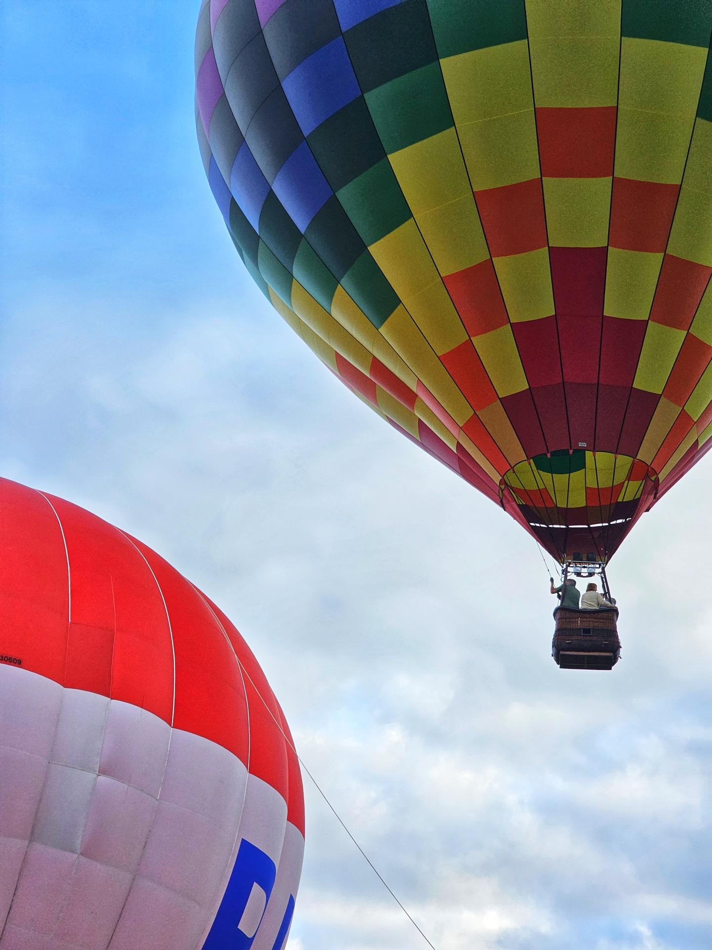 Colorful hot air balloons float in a cloudy sky.