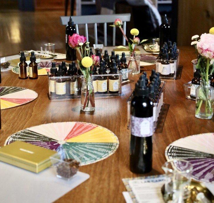 A table set with bottles, flowers, and colored scent wheels.