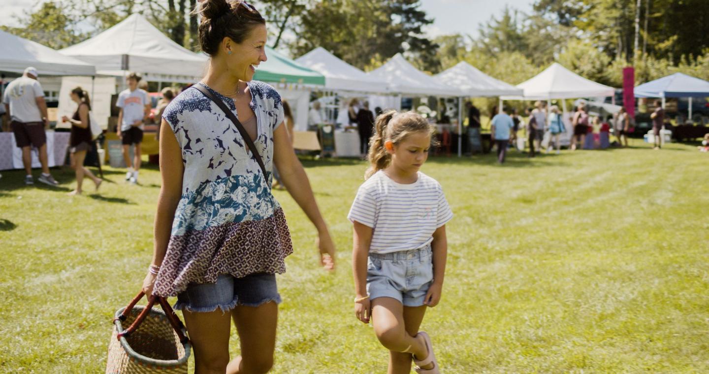 Mother and daughter walking at a sunny outdoor market.