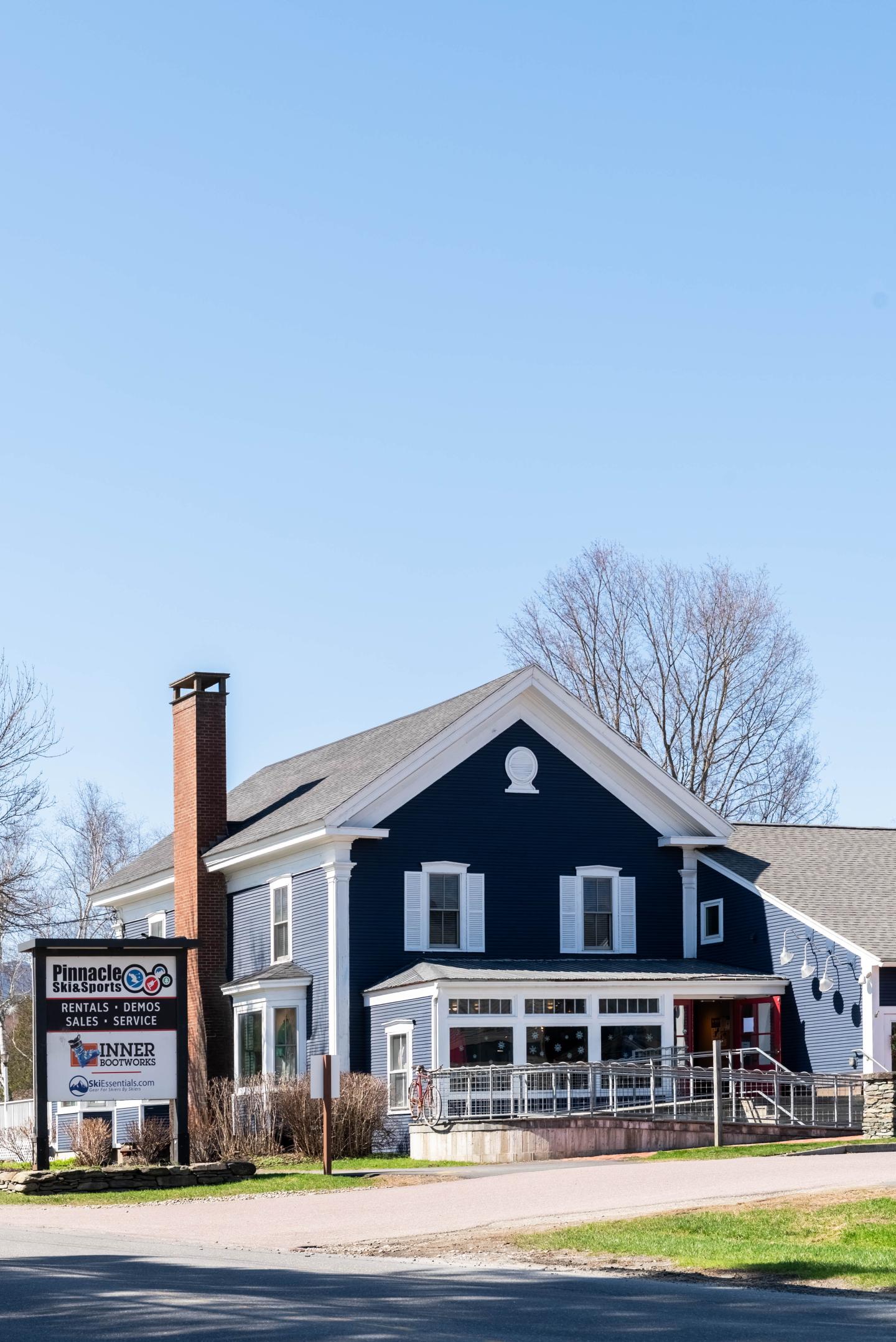 Blue house with white trim, sign in front, clear sky.