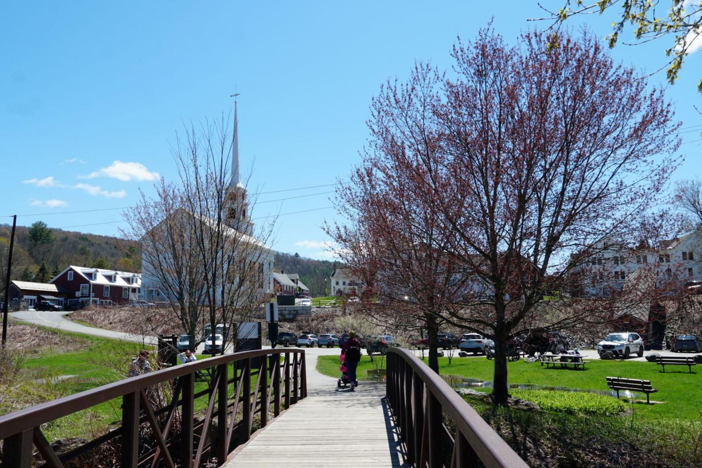 Bridge leading to a small town with church, trees, and blue sky.