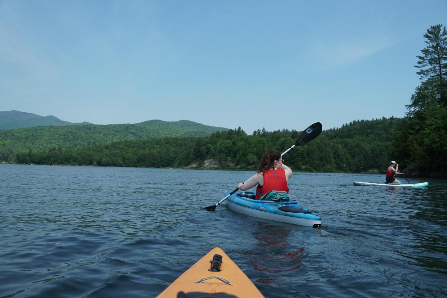 Kayakers paddling on a serene lake surrounded by forested hills.
