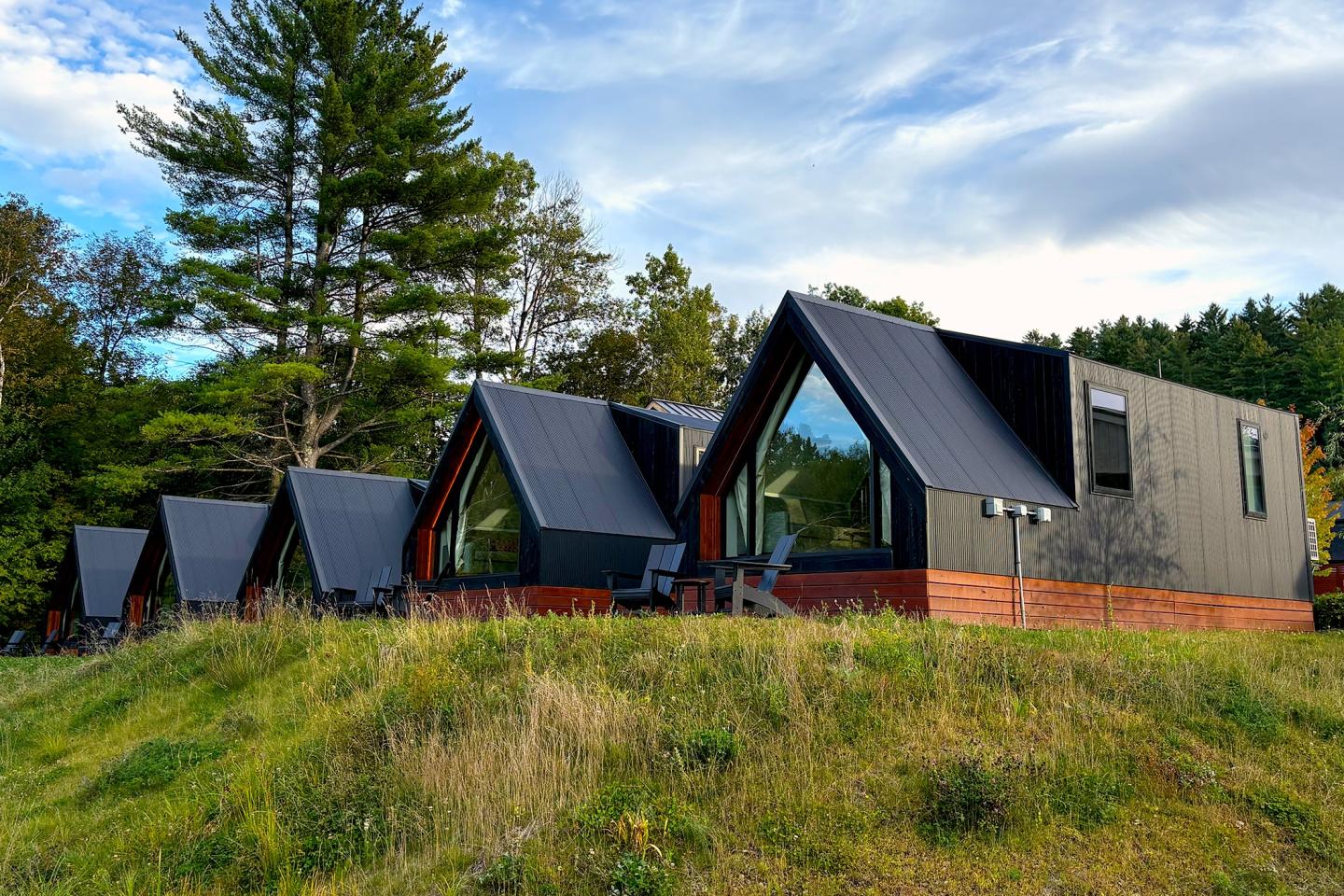 A-frame cabins on grassy hill under blue sky and trees.