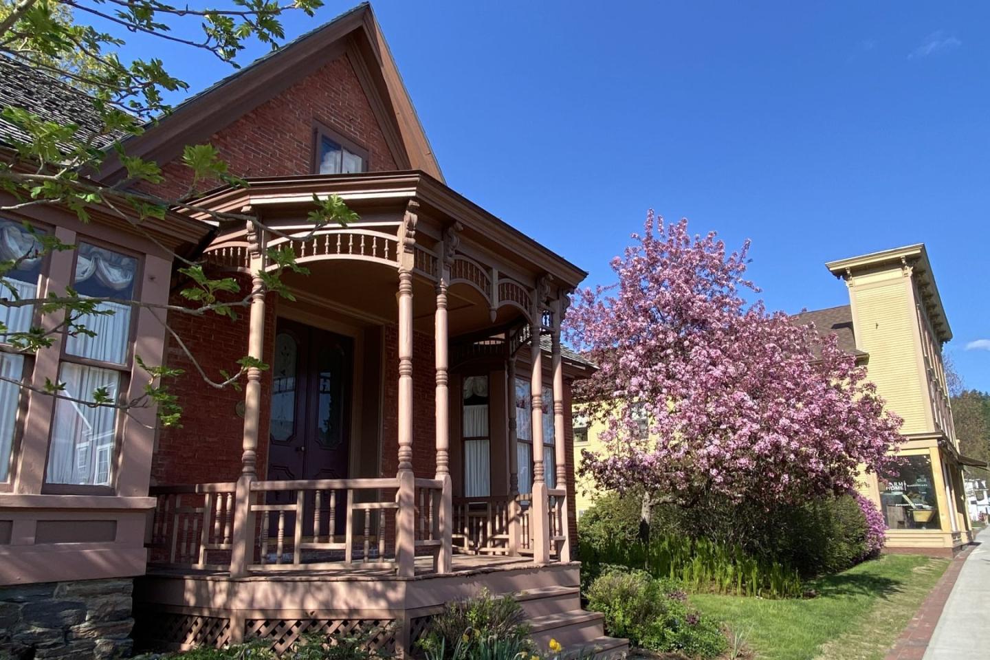Victorian house with porch, blooming tree, sunny day.