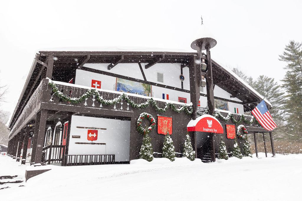 Snow-covered lodge adorned with flags and wreaths, surrounded by winter trees.