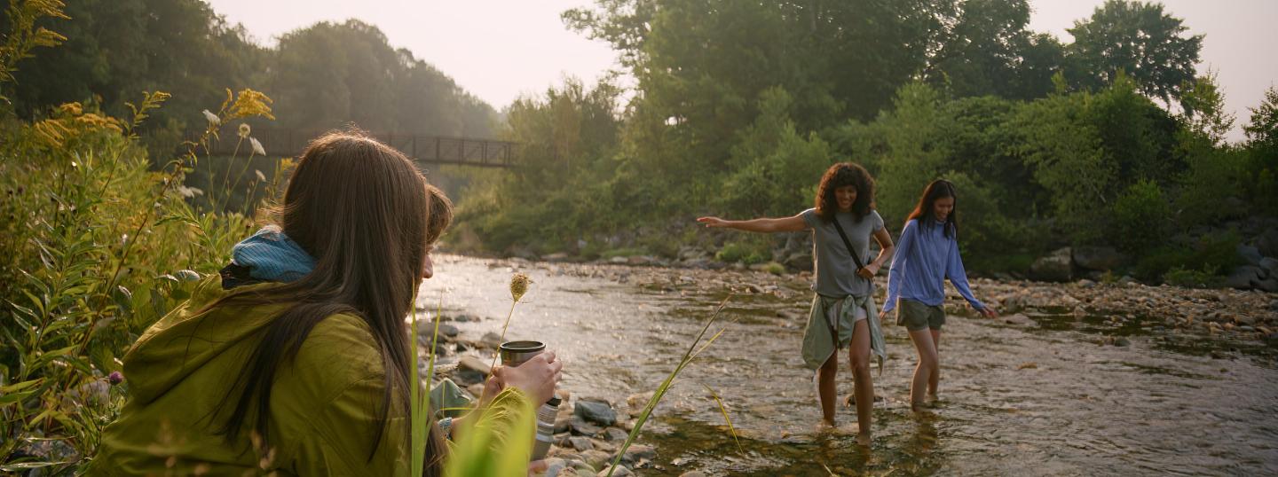Three people enjoying a walk along a serene, forested riverside in soft light.