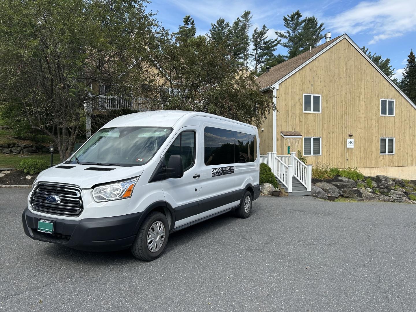 White van parked outside a beige building with trees in the background.