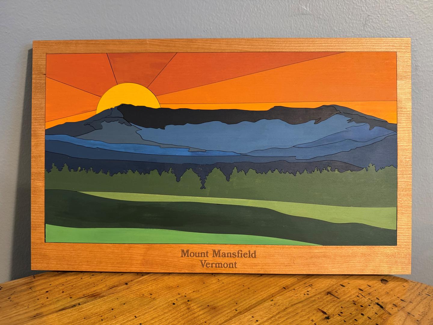 Sunset over layered mountain art piece with a wooden frame.