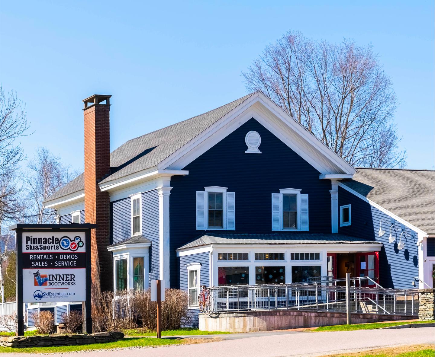 Blue house with white trim, red door, and a sign in front, clear sky in background.