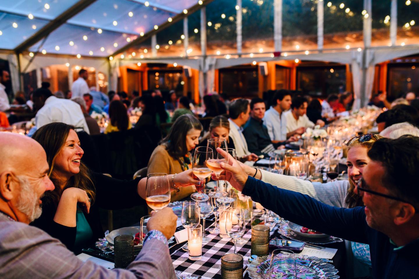Guests toast at a lively dinner event under string lights.